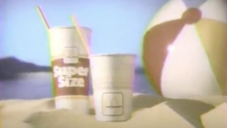 Two McDonald's cups set in sand beside a beach ball