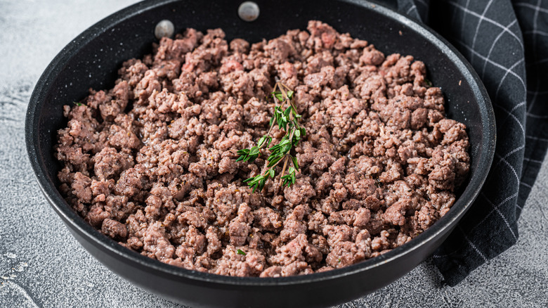 A skillet of fried ground beef with a sprig of thyme