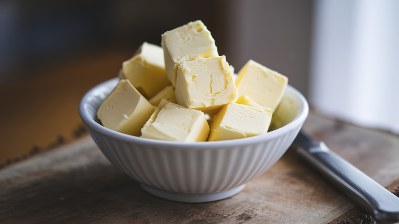 A small ceramic bowl is filled with rustic cubes of butter and sits next to a butter knife