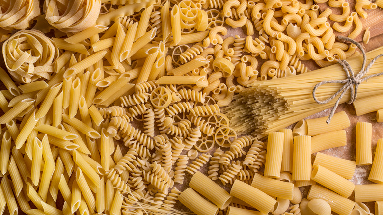 Different raw pasta shapes on wooden table