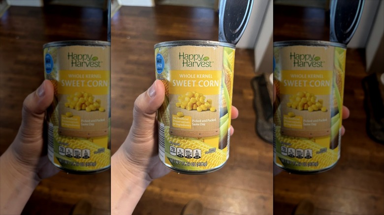 A hand holds a can of Aldi sweet corn