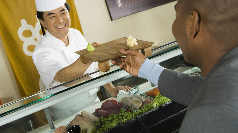 sushi chef handing diner ginger and wasabi on wood board
