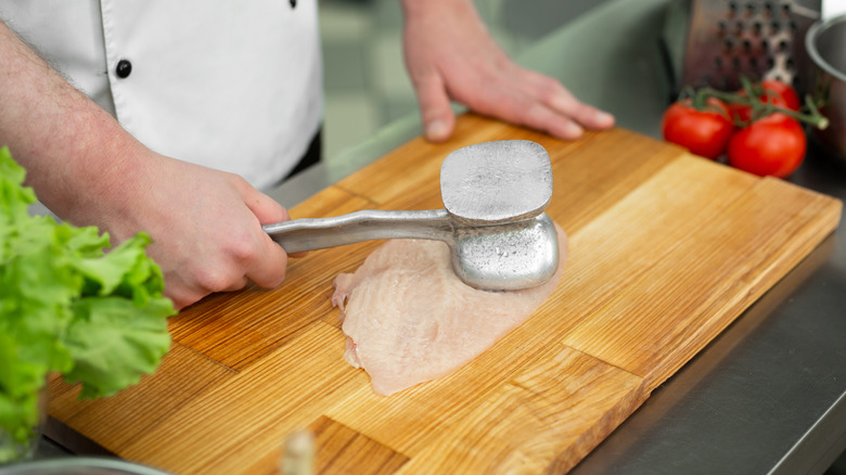 A chef hammering chicken on a cutting board