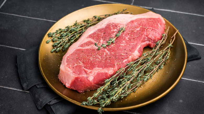 Raw New York strip on a plate with rosemary.