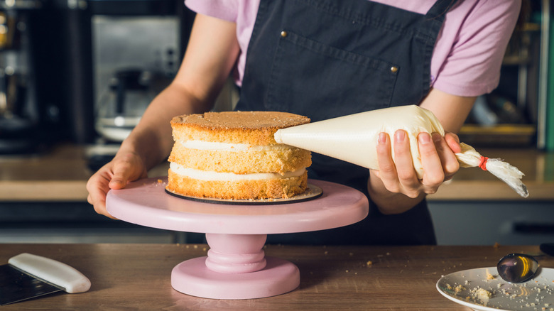 A person ices a cake with a piping bag.