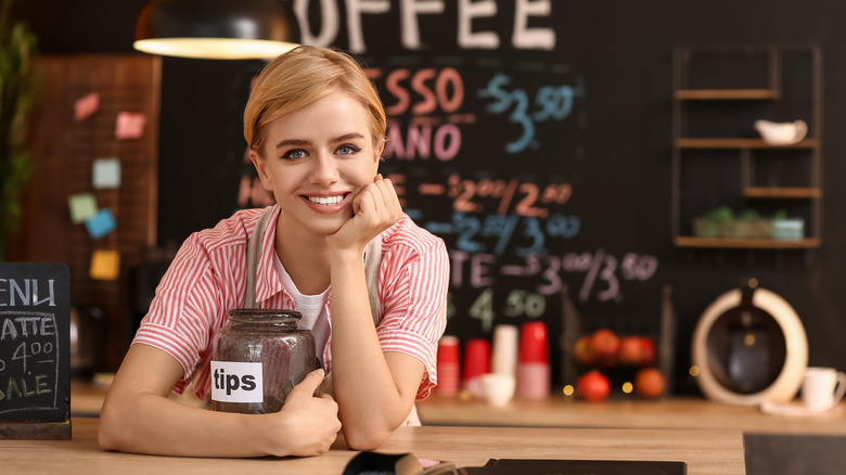 A barista in a coffee shop holding a tip jar