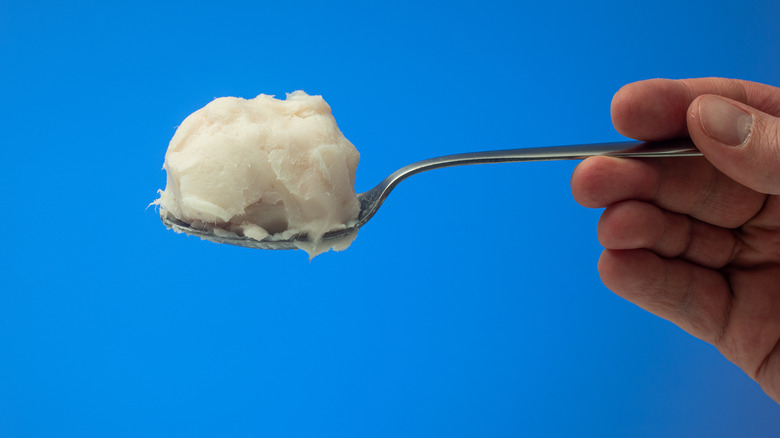 A hand holding up a spoonful of lard