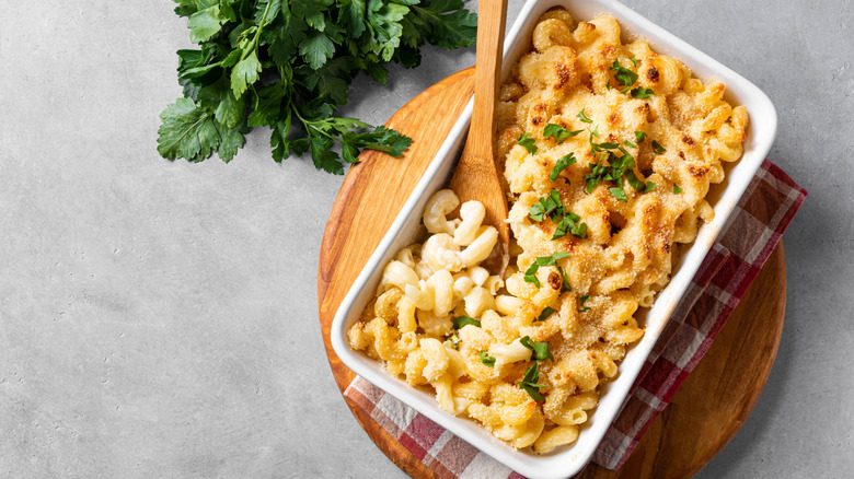 Mac and cheese sits in a casserole dish with breadcrumbs and fresh herbs on top