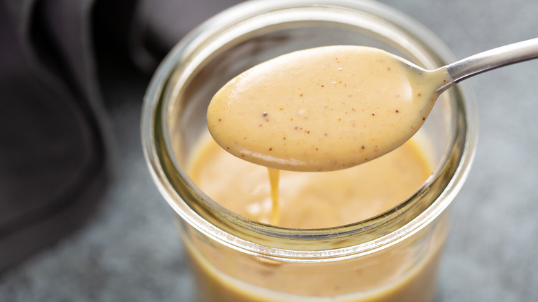 Someone spoons out a small bit of dressing from a small jar of homemade mustard vinaigrette