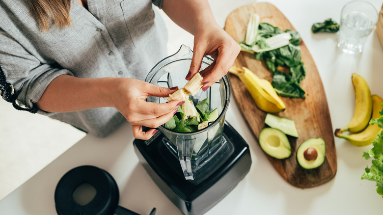 woman adding banana to a blender to make a smoothie