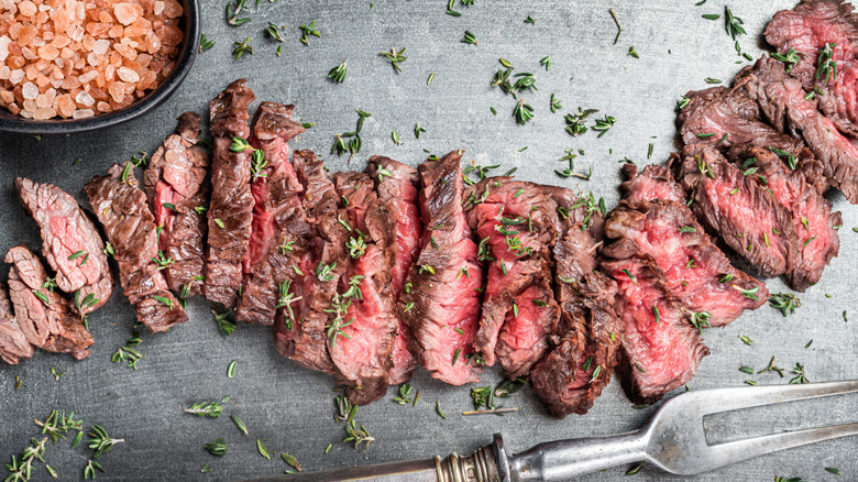 Skirt steak sliced and laid across a gray tabletop with rock salt