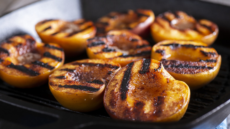 Halved grilled peaches on a grill topped with a sweet mixture