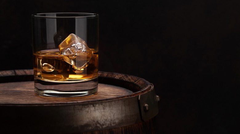 Scotch whiskey glass with ice on top of an old wooden barrel