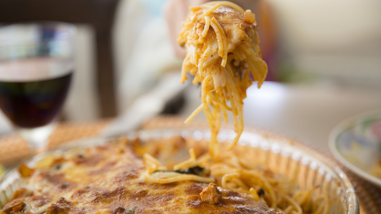 Someone takes a big scoop out of a pasta bake, with spaghetti and cheese dripping from a fork