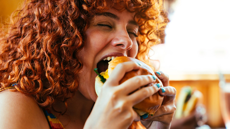 Customer with curly red hair enjoys a fast food burger