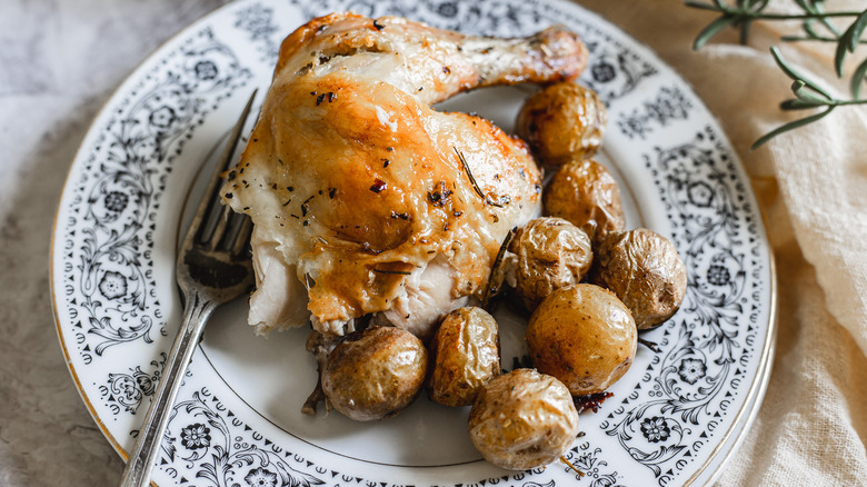 A Cornish hen quarter on a plate with baby potatoes and fork.