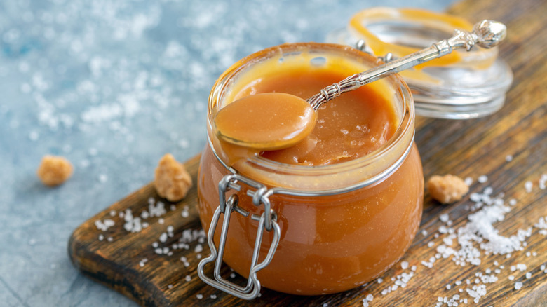 Homemade salted caramel sauce in jar and dripping off of a spoon .