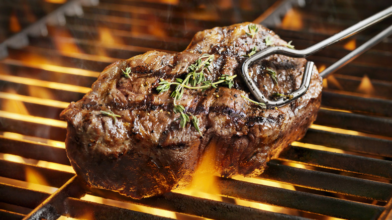 Tongs grabbing a steak on a grill