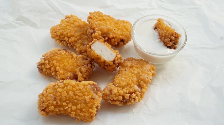 A plate of chicken nuggets next to a pot of sauce
