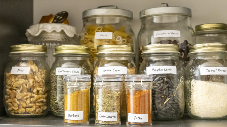 An array of glass jars in different sizes, with matching labels but varying lids and contents, sit on a shelf
