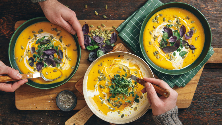 Three bowls of pumpkin soup with pumpkin seeds and fresh herbs.