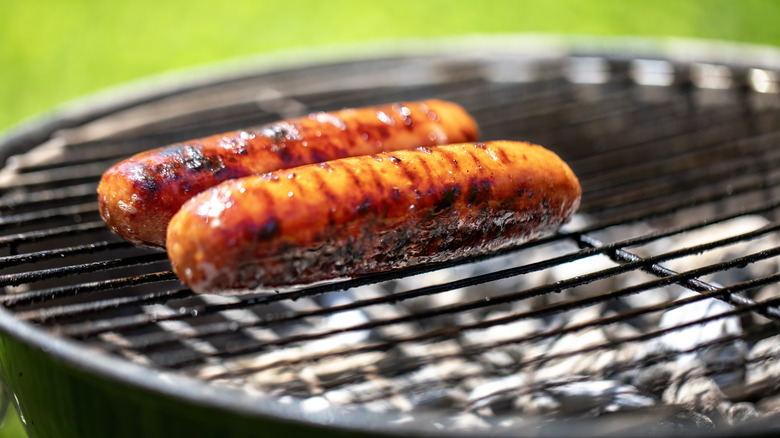 Two hot dogs roast on a grill