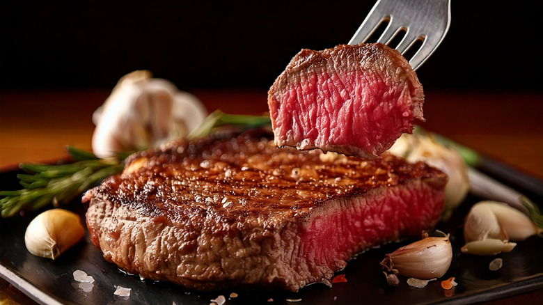 A fork spears a bite of meat cut from a steak