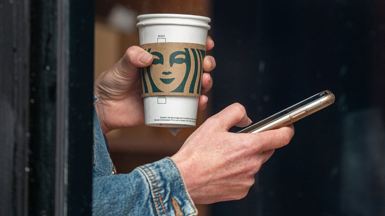 Customer holding Starbucks cup and using phone