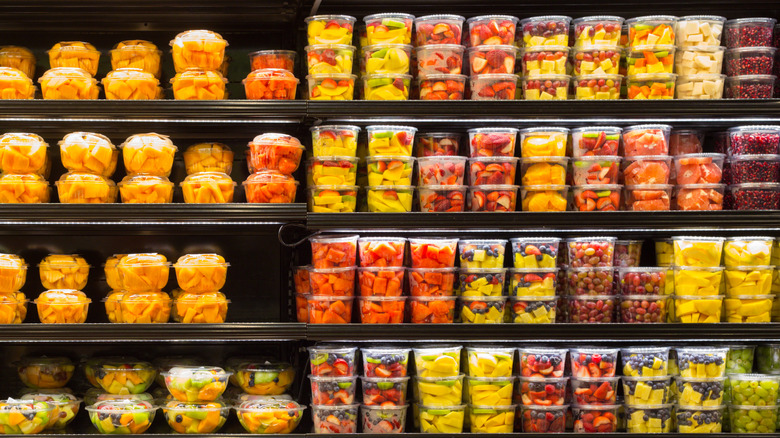 Refrigerated grocery store aisles filled with plastic tubs of pre-cut fruits.