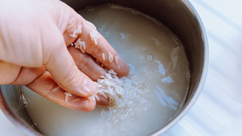 A hand washing rice in a bowl