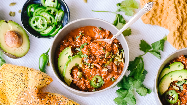Pumpkin and turkey chili in bowl on table with garnish