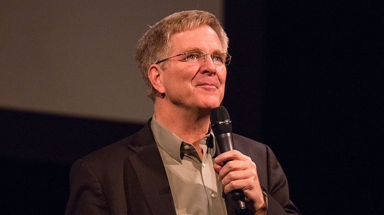 Rick Steves speaks on stage, looking up at the crowd