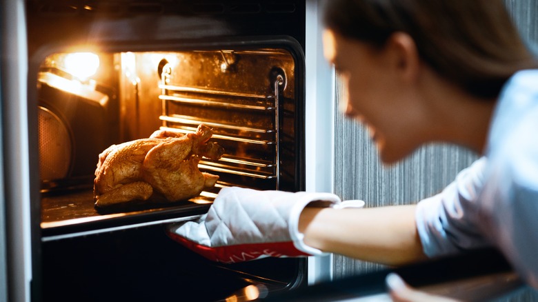 A woman taking a roast chicken out of the oven
