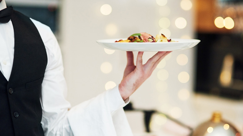 Waiter in tuxedo carrying a plate of food at a restaurant.