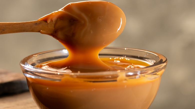 A wooden spoon is dipped into a small glass bowl of dulce de leche
