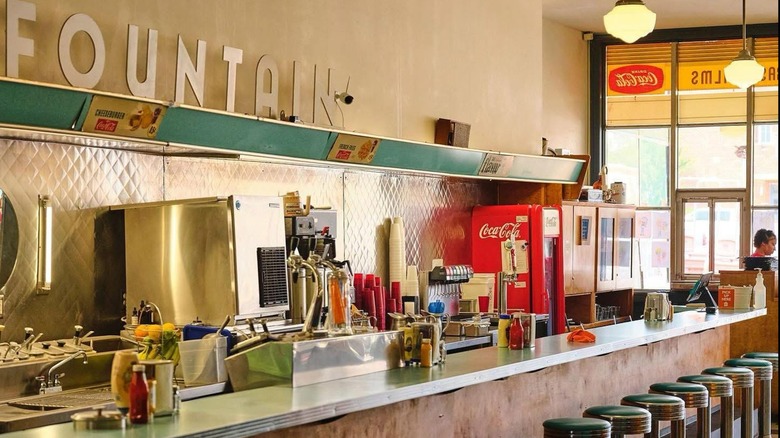 A vintage counter with chrome stools and a sign saying "Fountain" on the wall behind
