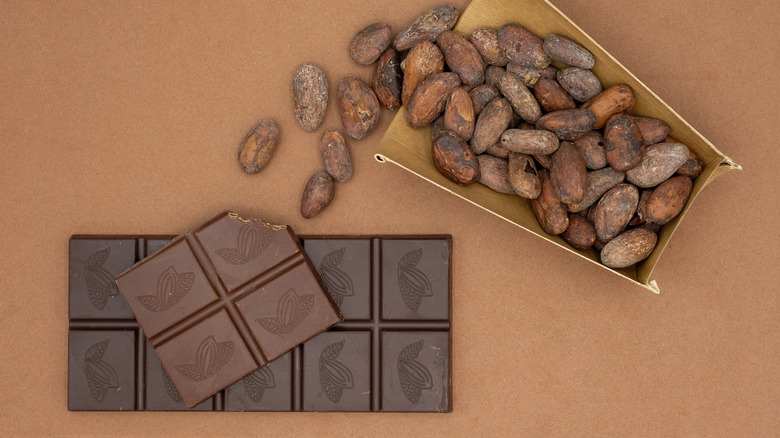 A large bar of chocolate alongside a pile of cocoa beans