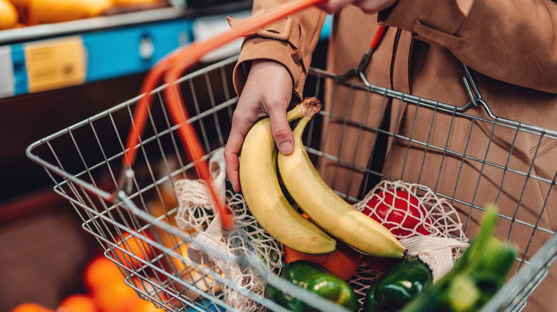 A photo of a shopper placing bananas in a shopping basket