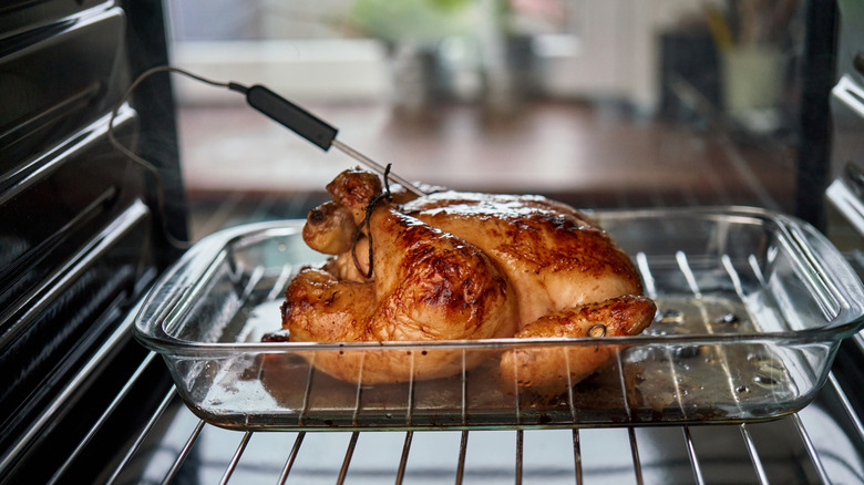 A chicken roasting in the oven with a meat thermometer in it