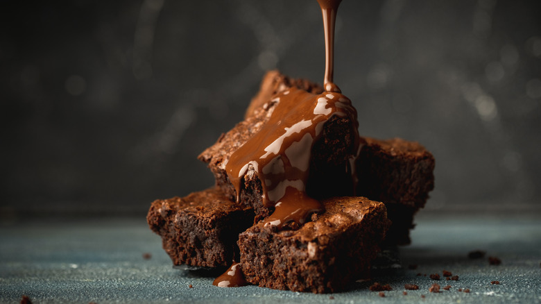Liquid chocolate is drizzled over four brownies sitting on a countertop
