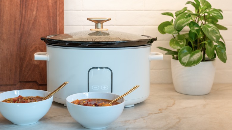 Slow cooker on the counter with two bowls of food in front of it