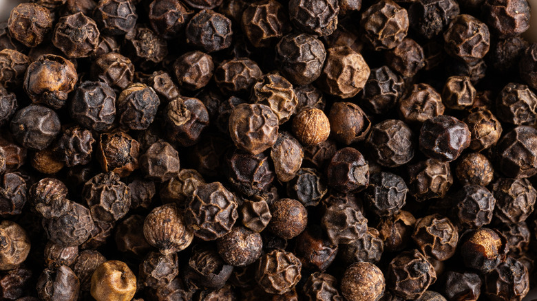 Many peppercorns rest in a pile in close-up, showing their unique texture.
