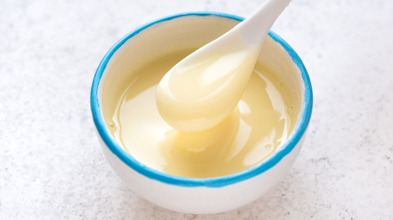 Bowl of sweetened condensed milk on table with a spoon inside of it