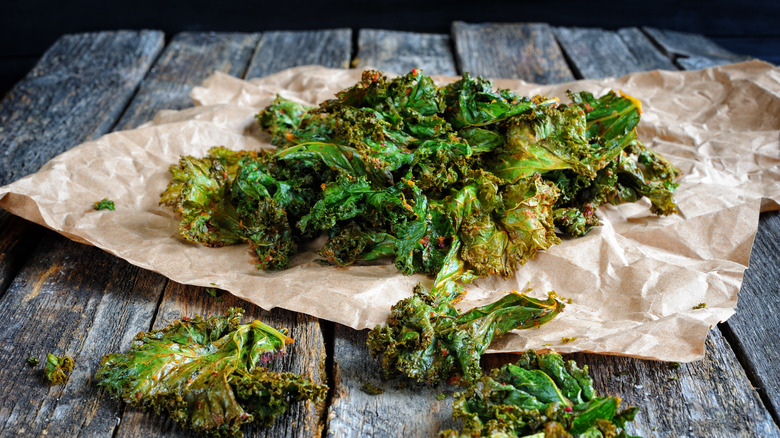 Oven-baked crispy kale chips sits on a crumpled piece of parchment paper