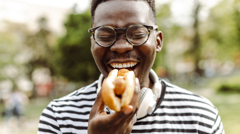 A person with glasses joyfully eats a hot dog