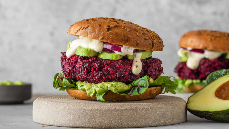 A beet burger with vegan mayonnaise, avocado, and onion on a white background.