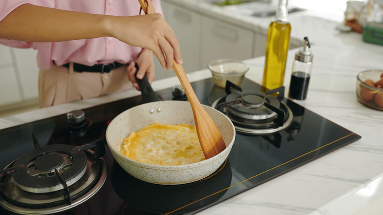 Person cooking omelet on stove with wooden spatula.