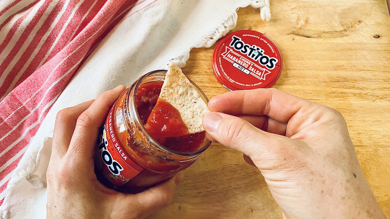 A hand dipping a tortilla chip in a jar of tostitos salsa