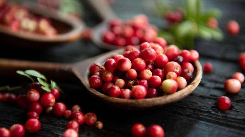 Cranberries in spoon and on wooden surface