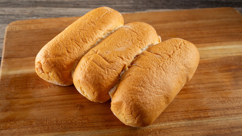 Three hot dog bun on a wooden cutting board